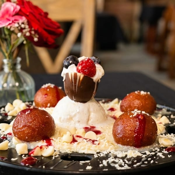 Gulab Jamun dessert with vanilla ice cream, chocolate shell, berries, and white chocolate chips.